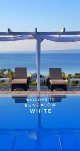 a pool with two lounge chairs under a welcome to burrow white sign at Bungalow White Tennis Apartments & Suites in Pefkochori