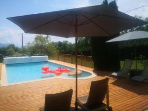 einen Pool mit einem Sonnenschirm und zwei Stühlen sowie einem roten aufblasbaren Pool in der Unterkunft L'oree des Bornes-appartement avec piscine in Évires