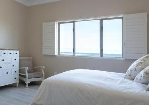 a bedroom with a bed and a chair and windows at Seafront Retreat in Sandbaai in Hermanus