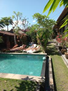 a pool with two people laying on chairs in a yard at Werkudara Guest House in Ubud