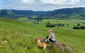 a woman sitting on a rock with a dog at Rockwood Karkloof Forest Lodge & Mountain Cabin in Yarrow