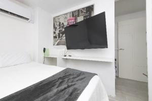 um quarto branco com uma cama e uma televisão na parede em AMANECER BOUTIQUE HOME, BEACH, Village & RELAX em Chiclana de la Frontera