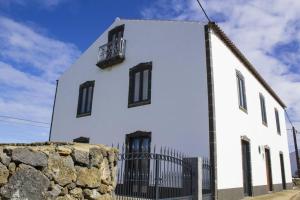 a white building with black windows and a stone wall at Casa Lagar de Pedra T3 in Santa Cruz da Graciosa