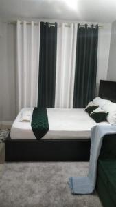 a bedroom with a bed with white and green curtains at Lux Suites Coral Bells Studio Apartments in Kiambu