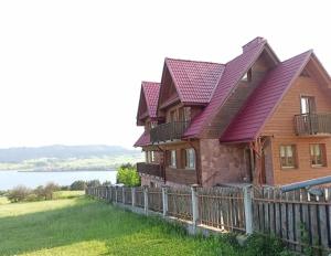 une maison en bois avec une clôture à côté d'un lac dans l'établissement CHATA MANIOWY Wyspa Ciszy nieopodal Czorsztyna, Maniowy i Kluszkowce nad Zalewem Czorsztynskim, à Maniowy