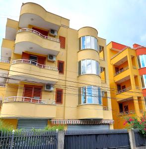 a yellow building with red windows and a fence at Apartments Vila Cala in Durrës