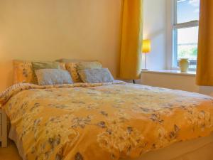 a bedroom with a bed with a yellow comforter and a window at Hatters Croft in Cockermouth