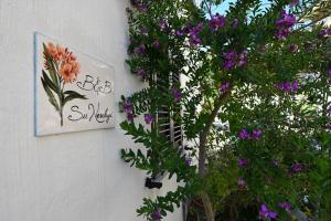 a tree with purple flowers and a sign on a wall at B&B Su Neulagi in Triei