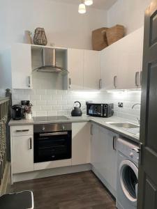 a kitchen with white cabinets and a washer and dryer at Shakespeare's Snug in Prescot