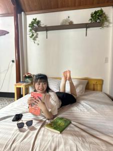 Una chica acostada en una cama con un libro en Homestay San Hô, en Dong Hoi