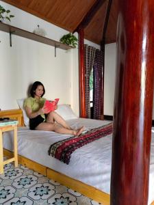 una mujer sentada en una cama leyendo un libro en Homestay San Hô, en Dong Hoi