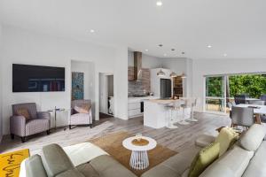 a white living room with a couch and a kitchen at Our Happy Place - Waihi Beach Holiday Home in Waihi Beach