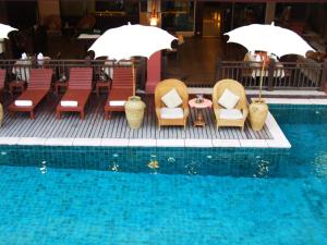 a pool with chairs and tables and umbrellas next to a swimming pool at Sarita Chalet & Spa Hotel - SHA Extra Plus in Jomtien Beach