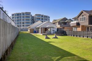 um quintal relvado com casas ao fundo em The Iconic Kiwi Bach, Full Site Downtown Mount em Mount Maunganui