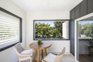 a dining room with a wooden table and two windows at Aura Apartment-LJHooker Yamba in Yamba