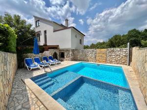a swimming pool with two chairs and a house at Apartman Milly in Grižane