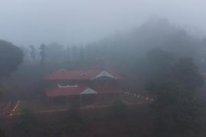 a house on a hill in the fog with lights at Regal Retreat by VEO - Part of StayVista in Wayanad