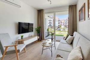 a living room with a couch and a tv at Flatbook Apartamenty - Sztutowo Baltic Garden in Sztutowo