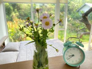 a vase with flowers and an alarm clock on a table at Royal mountain view (วิวเขาหลวง) in Ratchaburi