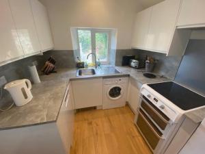 cocina con armarios blancos, fregadero y lavavajillas en Ivybridge Cottage, en Ivybridge