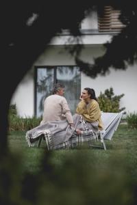 Ein Mann und eine Frau sitzen auf einer Bank im Gras in der Unterkunft Shuum Boutique Wellness Hotel in Kołobrzeg