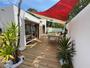 une terrasse en bois avec une table et un parasol rouge dans l'établissement Mini Villa Indépendante à 350m de la mer (LAX), à Lucciana