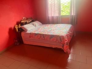 un piccolo letto in una camera rossa con finestra di A&G Guest House a Kumba