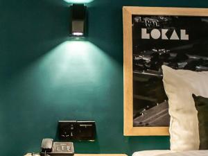 a room with a green wall with a bed and a lamp at LOKAL Rooms x Shahrah-e-Faisal (Nursery) in Karachi