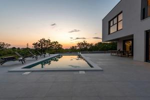 a building with a pool with a sunset in the background at Villa Rocinante ZadarVillas in Murvica