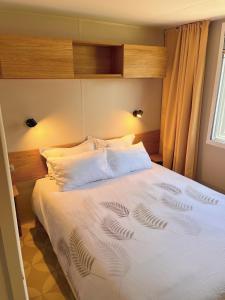 1 dormitorio con 1 cama con sábanas y almohadas blancas en Mobil home camping 4 étoiles les Viviers 2 chambres en Lège-Cap-Ferret
