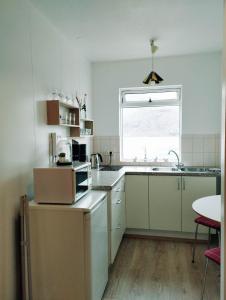 eine Küche mit weißen Schränken, einem Waschbecken und einem Fenster in der Unterkunft Gistiheimilið Bergistangi 1 in Norðurfjörður