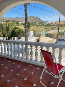einem roten Stuhl auf einer Veranda mit weißem Geländer in der Unterkunft Casa Rural Los Caballos Finca Canca Alora Caminito del Rey in Alora