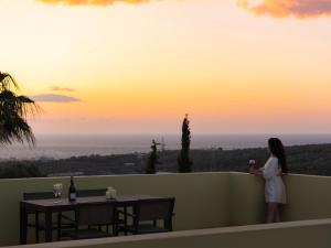 kobieta stojąca na balkonie z widokiem na zachód słońca w obiekcie Mela Villas w mieście Maroulás