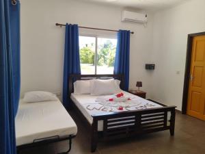 1 dormitorio con 2 camas, cortinas azules y ventana en Le Nid de Bea Self-catering Apartments en La Digue