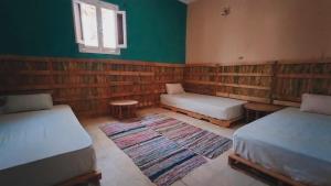 a room with two beds and a couch and a rug at هوستل أجبناخ إنشالي Hostel Agbenakh Inshaly in Siwa