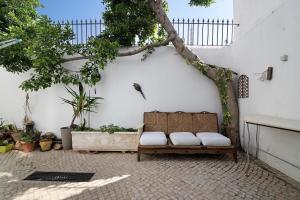 un banco sentado junto a una pared blanca con un árbol en Casa da Cidade de Loulé en Loulé