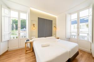 a white bedroom with a bed and two windows at Hotel Alda Triacastela in Treacastela