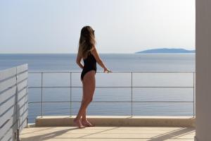 a woman standing on a balcony looking out at the water at Manificus Villas, Designed for Togetherness, By ThinkVilla in Palaiokastro
