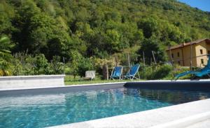 a swimming pool with two blue chairs and a house at Casa Fontanera in Gravedona