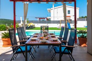 a dining table and chairs on a patio with a pool at Villa Plenča green sea near to the sea - heated pool in Šibenik