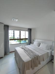 a white bedroom with a large bed and a large window at Loft Luxor Tambaú in João Pessoa
