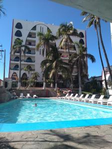 a pool in front of a large building with palm trees at Hotel Essen's in Mazatlán