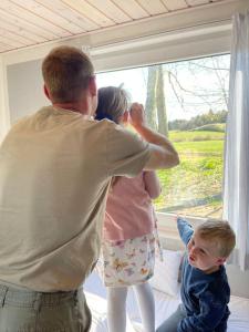 Un uomo e due bambini che guardano fuori da una finestra di Tiny House i storslået natur a Frederikshavn