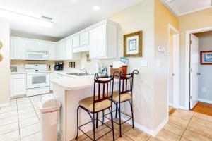 a kitchen with white cabinets and two chairs at a counter at Three C's 202 in Gulf Shores