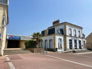 a white building with a palm tree in front of it at Le cosy in Courseulles-sur-Mer