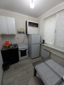 a small kitchen with white appliances and a table at ОРАНЖЕВЫЙ МИР in Aktobe