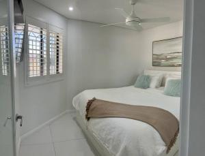 een witte slaapkamer met een bed en een plafondventilator bij Bondi Beach Waves Beachfront Apartment in Sydney