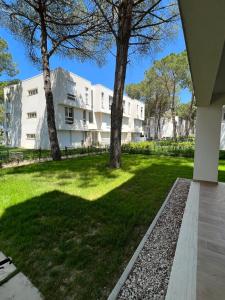 un grande edificio bianco con alberi nel cortile di Pine Apartments at San Pietro Resort a Durrës