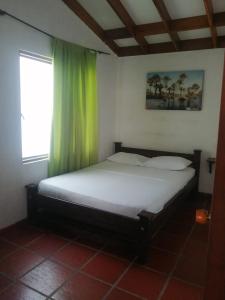 1 dormitorio con 1 cama con cortinas verdes y ventana en Cabañas El Samán Villavicencio, en Villavicencio