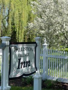 una señal para una posada del pueblo al lado de una valla blanca en Williston Village Inn en Burlington